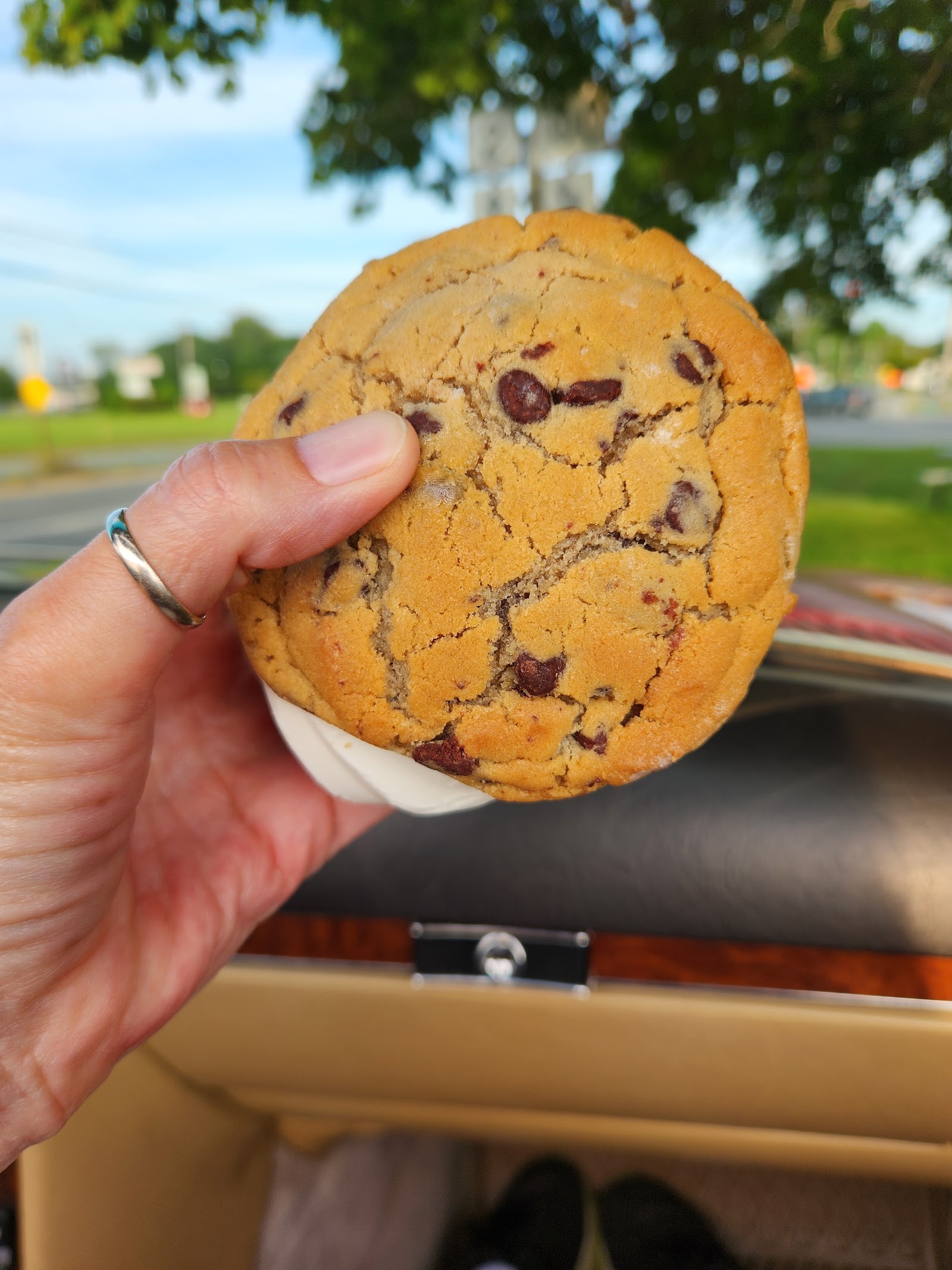 A hand holding a thick chocolate chip cookie ice‑cream sandwich outside the stand.