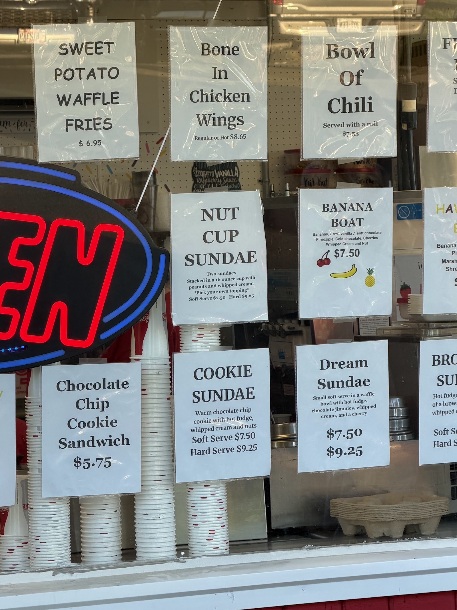 Close‑up of the sundae and shake signs taped inside the window, beside stacks of paper cups.