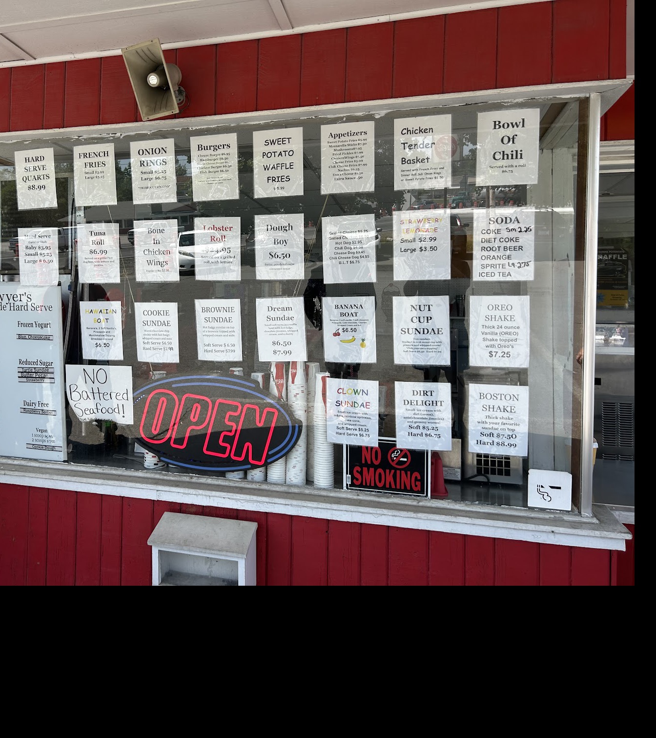 The walk‑up window covered edge to edge with Sawyer’s printed menu signs and a lit OPEN sign.