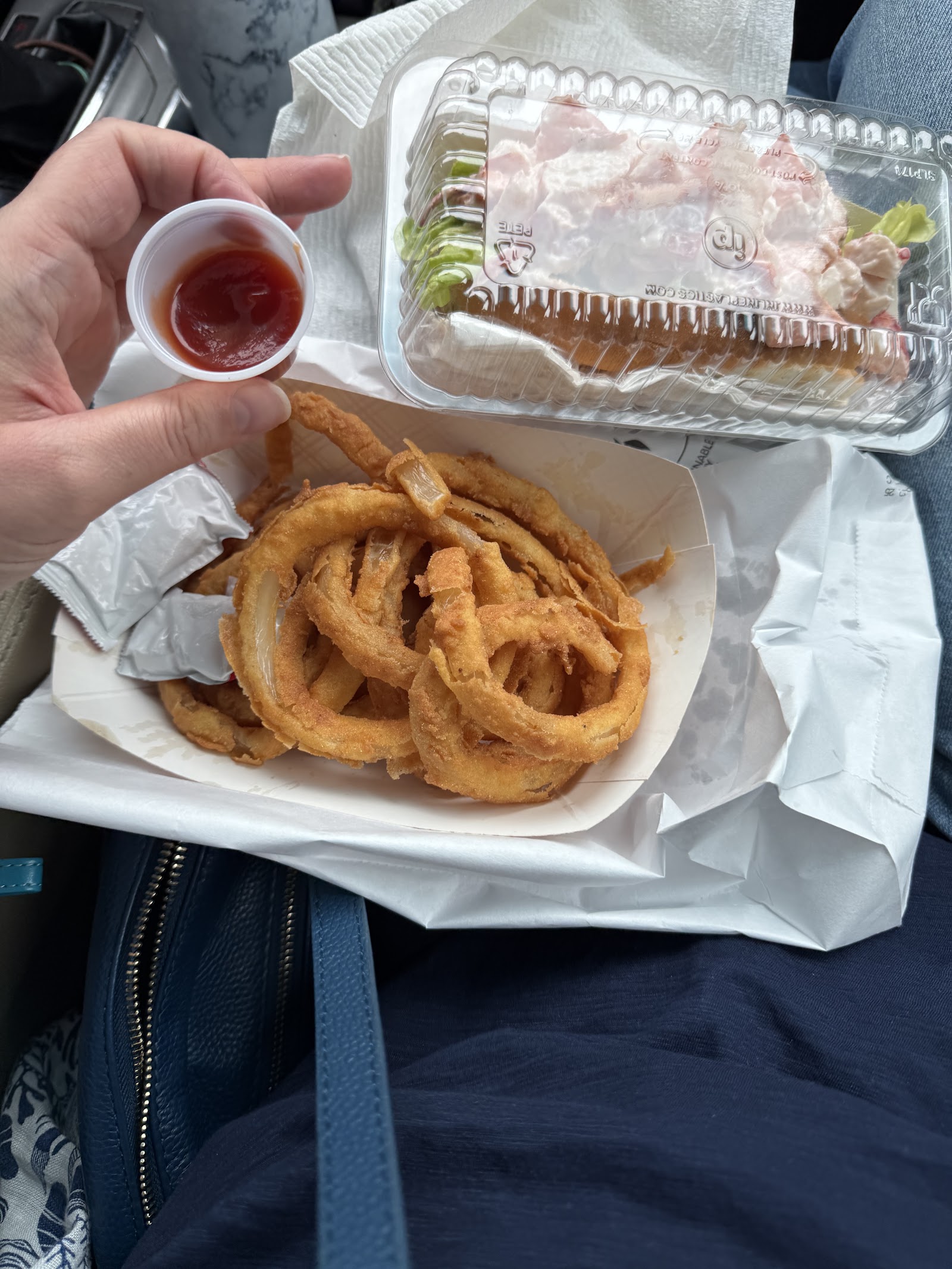 A basket of golden fresh‑cut onion rings with a cup of ketchup.