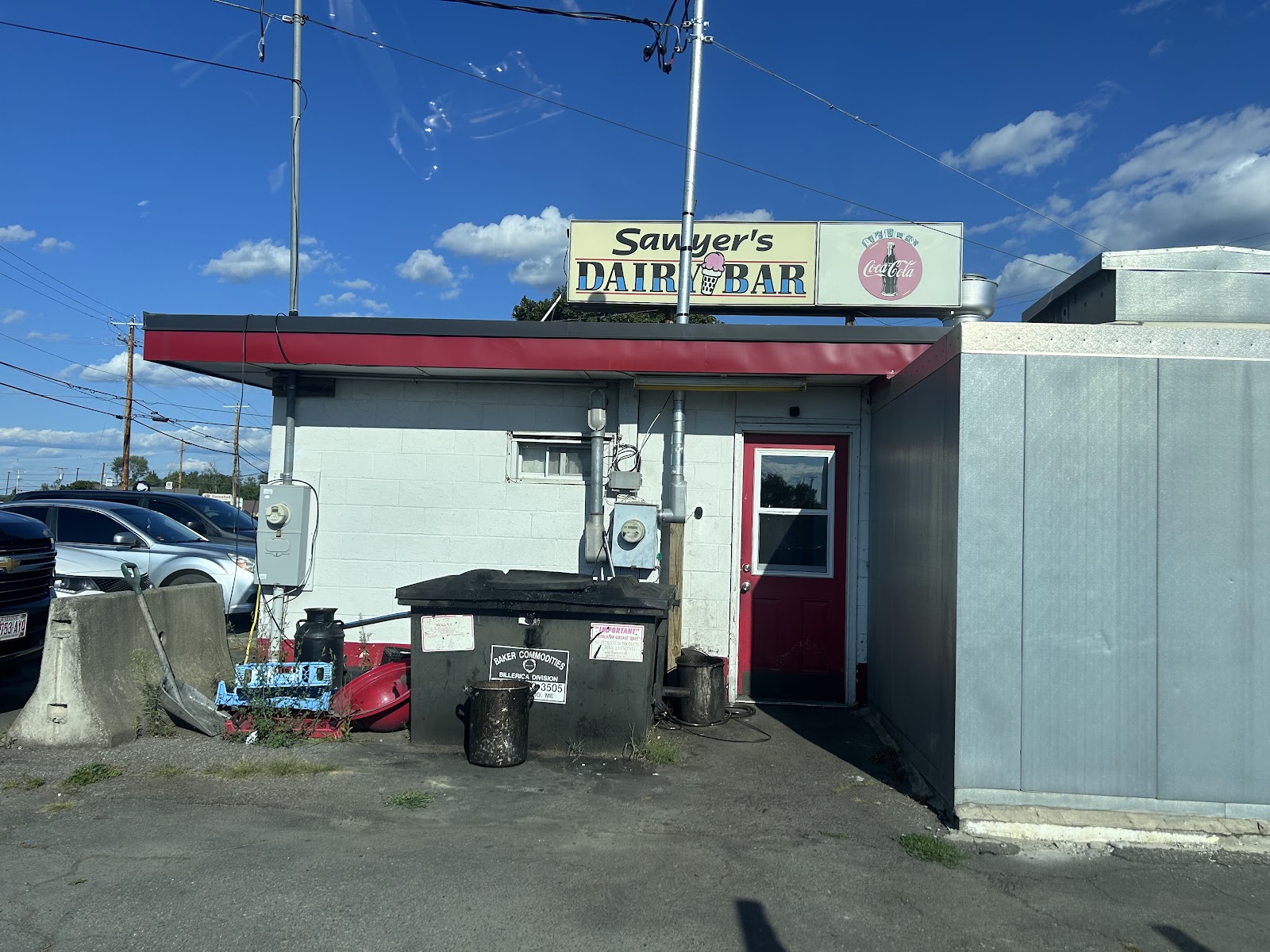 The Sawyer’s Dairy Bar sign and a red side door on the white cinder‑block building under a clear sky.